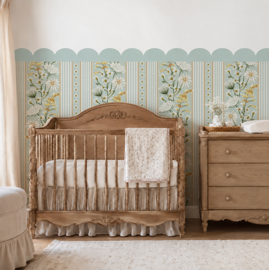 A styled nursery interior featuring a light wood crib with a white ruffled bedding set and a matching wooden dresser, set against a wall with vertical floral wallpaper and a scalloped border.
