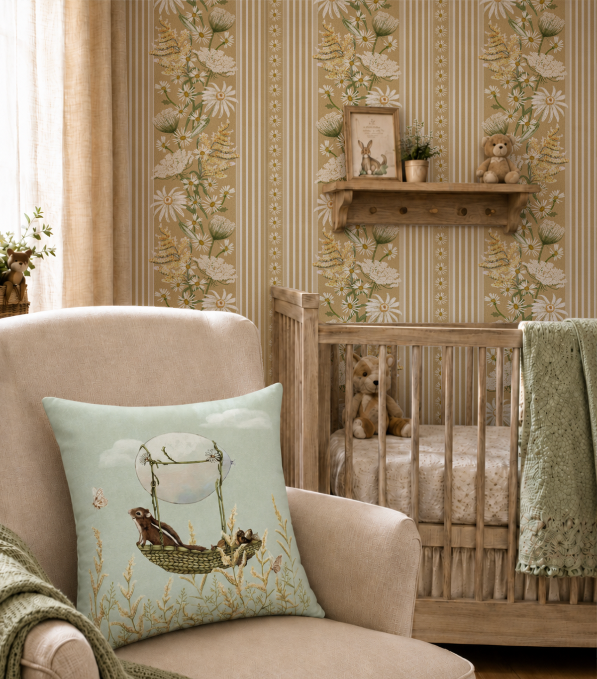 A styled nursery interior featuring a light blue throw pillow with a hot air balloon and chipmunk illustration, placed in front of a beige armchair. A wooden crib with a teddy bear sits beside the chair against a wall with striped and floral wallpaper.
