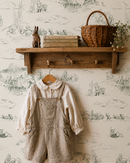 Children's outfit with overalls and shirt hanging on a wooden shelf against a pooh wallpapered wall.